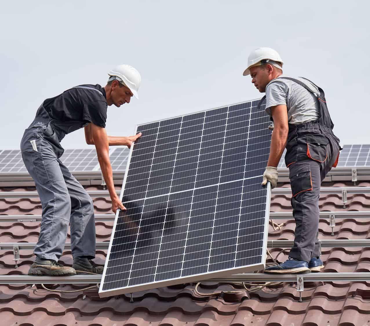 Installers placing a solar panel on a tile roof
